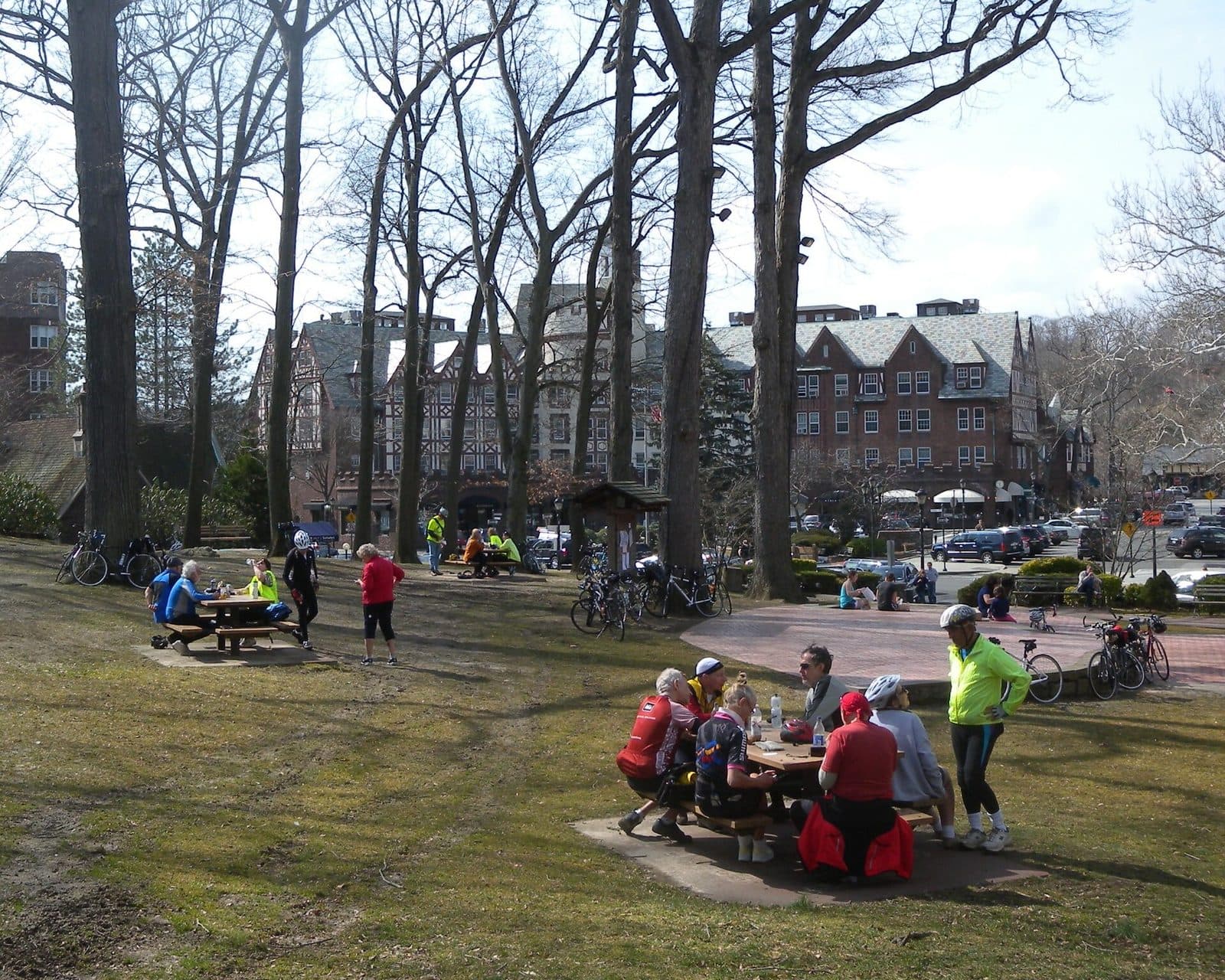 People at picnic tables in a small park in Scarsdale's village center, with Tudor-style shops behind